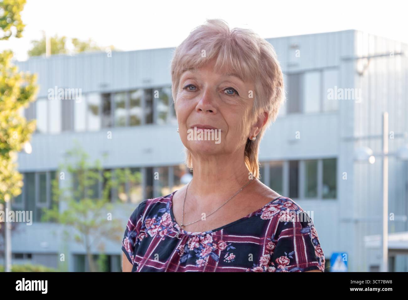 Une femme âgée de 65-70 ans dans une robe colorée se tient sur un quai de la gare. Banque D'Images
