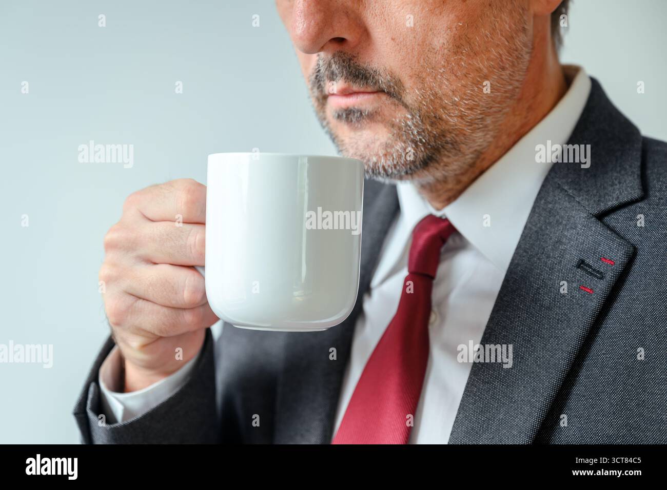 Gros plan de l'homme d'affaires tenant la tasse de café blanc près de la fenêtre du bureau, la routine du matin et le style de vie du lieu de travail. Mise au point sélective. Banque D'Images