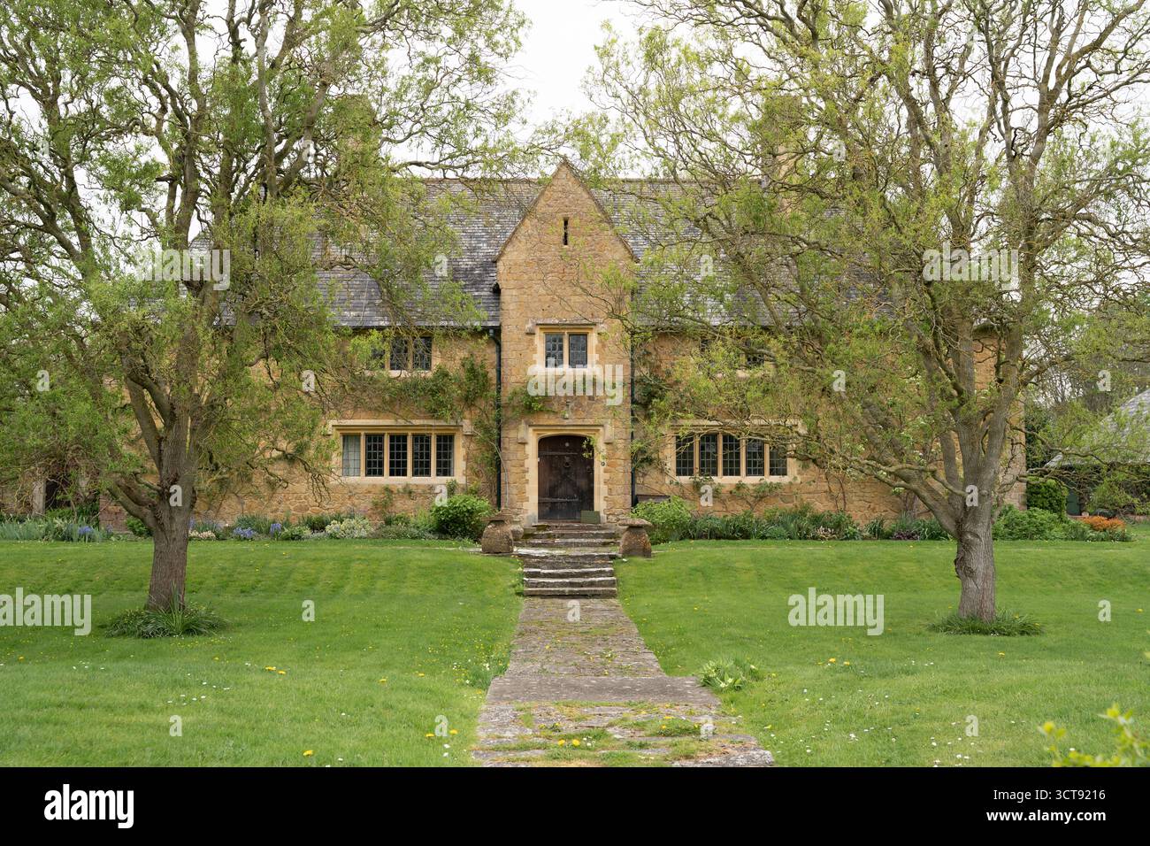 Élégante maison en pierre Cotswold avec arbres matures et pelouse bien entretenue au printemps Banque D'Images
