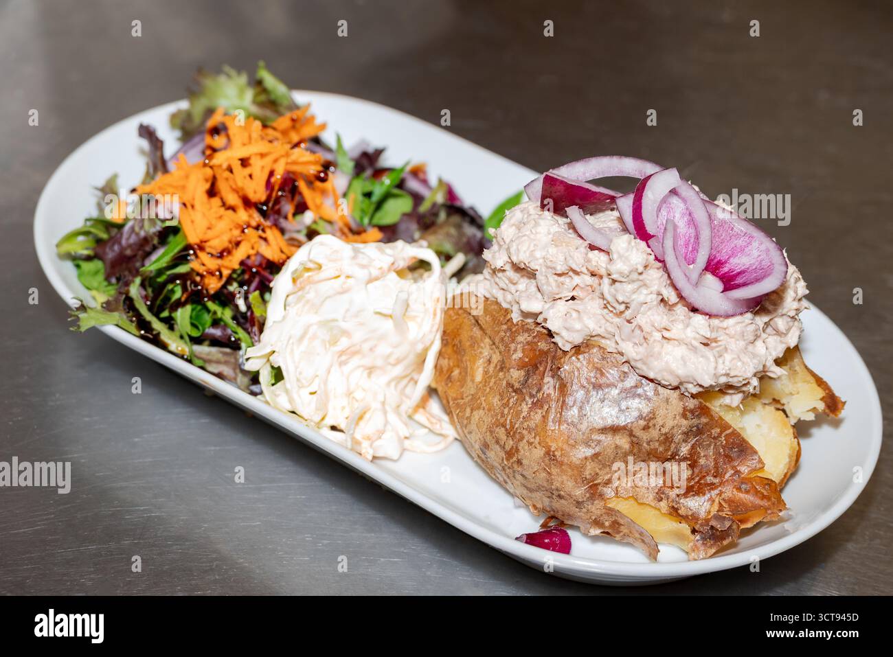 Dégustez un déjeuner de pommes de terre cuites au four ! Nappé de thon et d'oignon rouge, servi avec du coleslaw et une salade fraîche. Un repas savoureux et satisfaisant. Banque D'Images