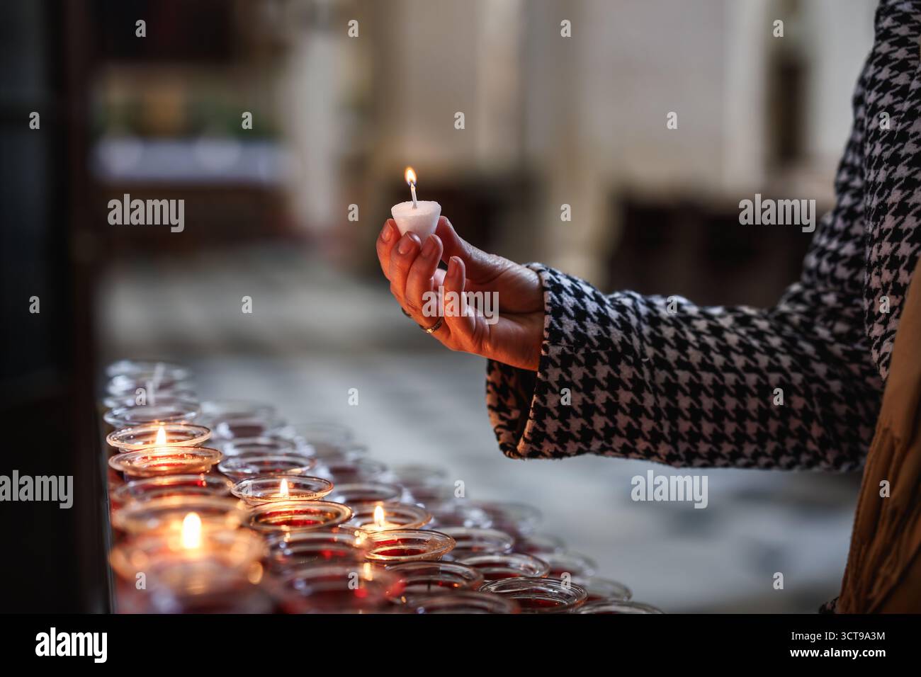 Femme allumant des bougies pour la prière à l'église. Acte symbolique de foi, de souvenir et de tradition religieuse Banque D'Images