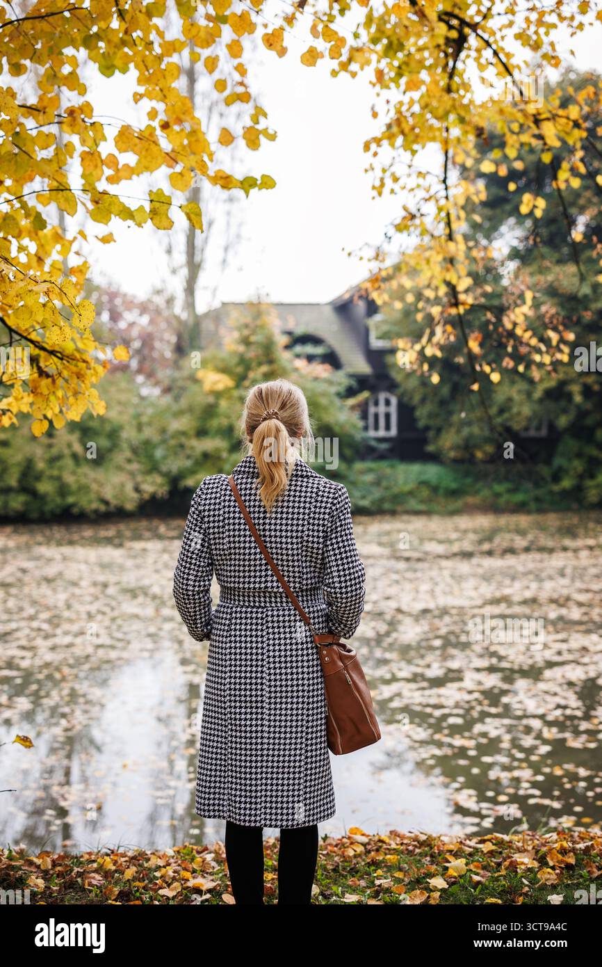 Femme réfléchie debout dans le parc d'automne, exprimant la mélancolie et l'humeur pensive de la solitude Banque D'Images
