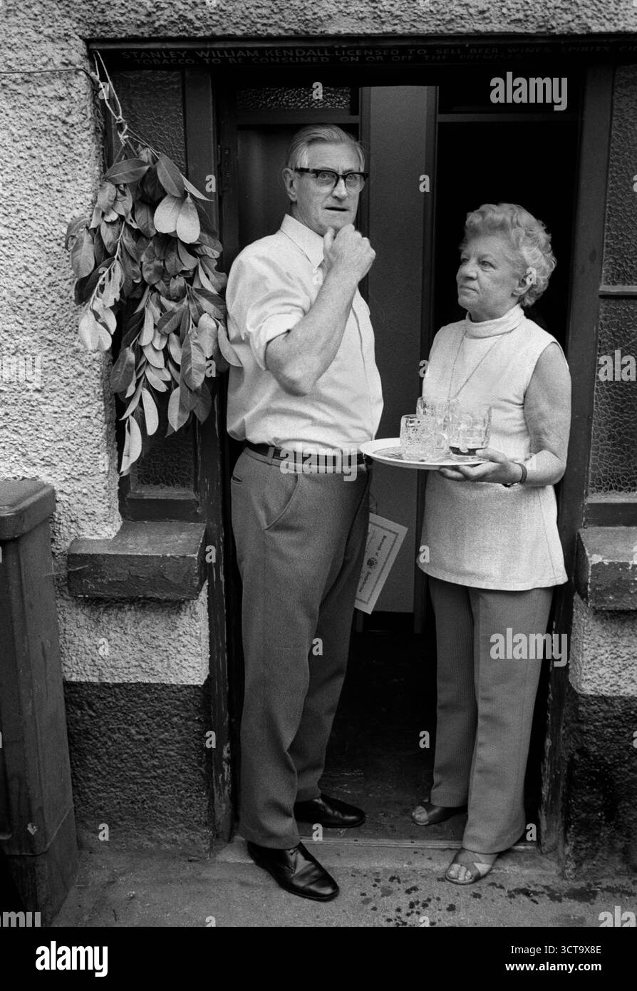 Ashburton court Leet est maintenant largement cérémoniel. Le tribunal manoir Leet traitait des infractions mineures dans la communauté et appliquait les règlements concernant la qualité des aliments de base, tels que le pain et la bière. Le publicain Stanley Kendall et sa femme, avec des verres à bière vides. Un brin de verdure est accroché à la porte du pub, pour indiquer que la bière a été goûtée et considérée comme propre à la consommation. Ashburton, Devon, Angleterre juillet 11975 1970s Royaume-Uni. HOMER SYKES Banque D'Images