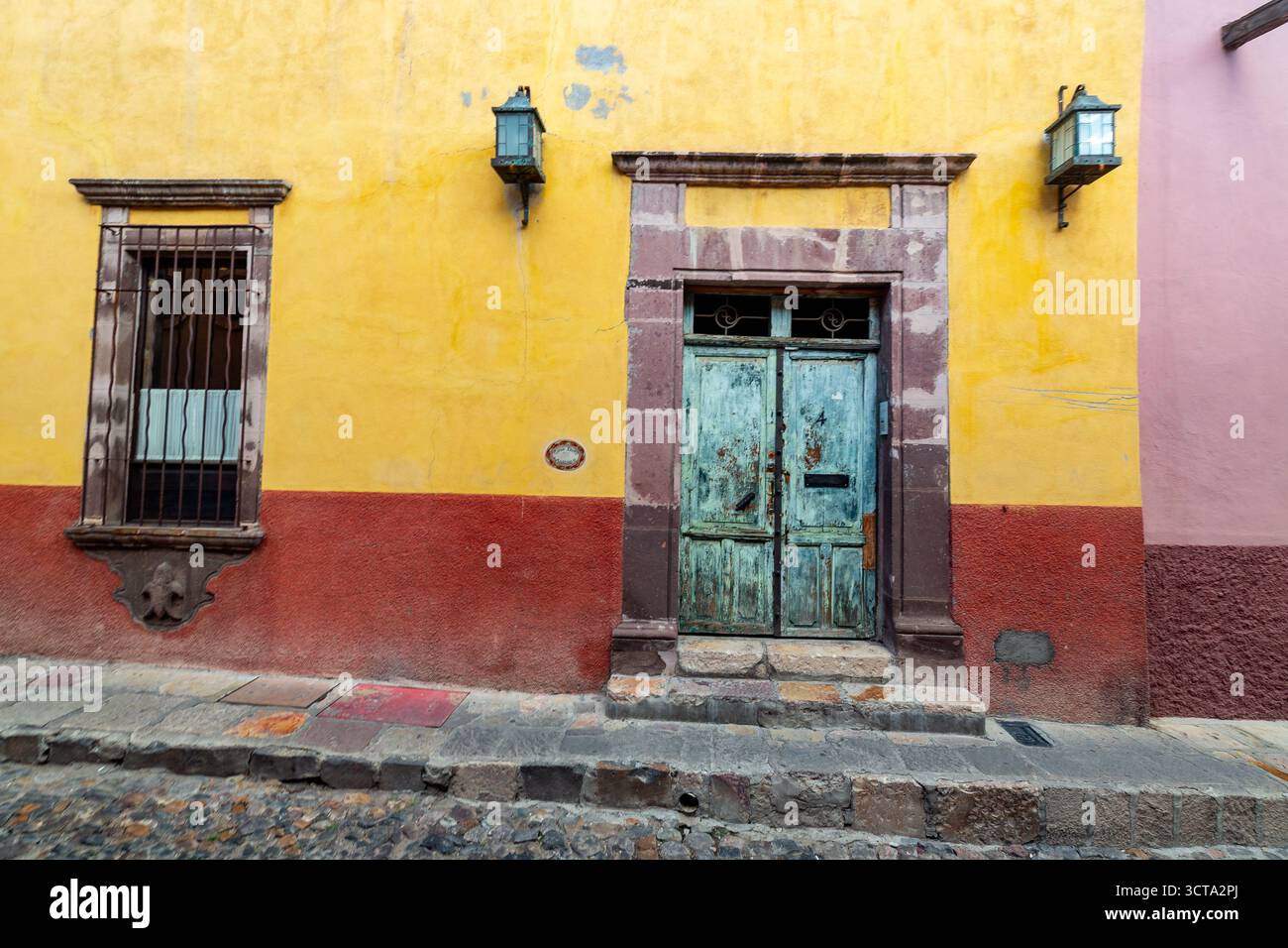 Une façade colorée de bâtiment comprend une fenêtre avec des barres, une porte bleue altérée et des lanternes, mettant en valeur le style architectural unique de la région. Banque D'Images