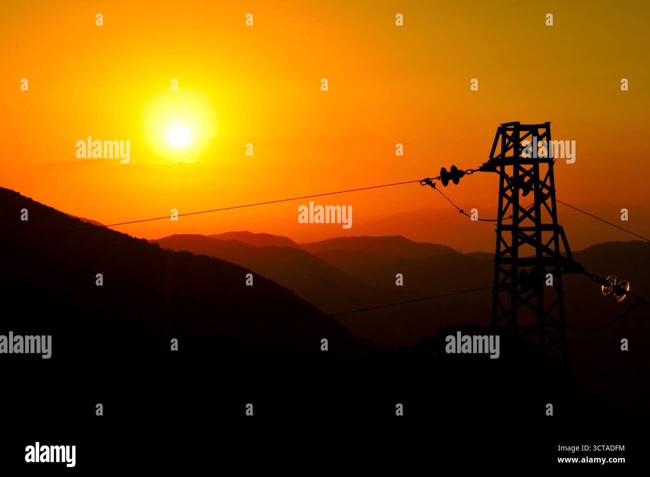 Coucher de soleil doré avec tour de puissance et silhouettes de montagne – énergie et nature en contraste visuel Banque D'Images