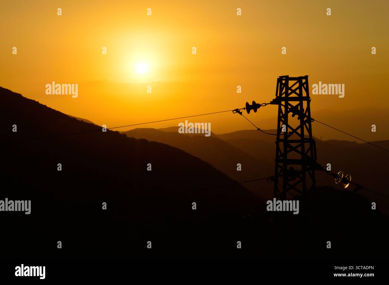 Coucher de soleil doré avec tour de puissance et silhouettes de montagne – énergie et nature en contraste visuel Banque D'Images