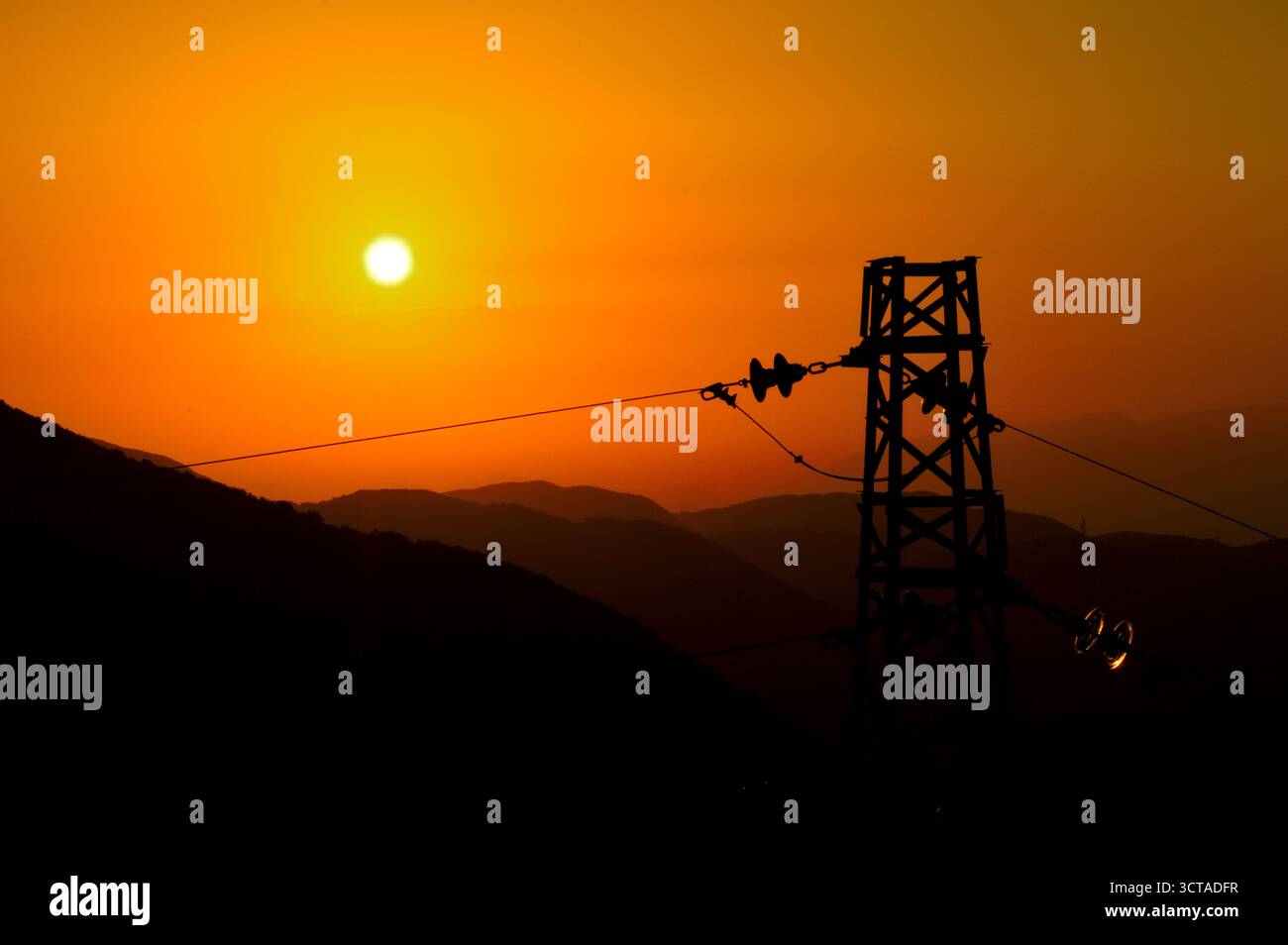 Coucher de soleil doré avec tour de puissance et silhouettes de montagne – énergie et nature en contraste visuel Banque D'Images