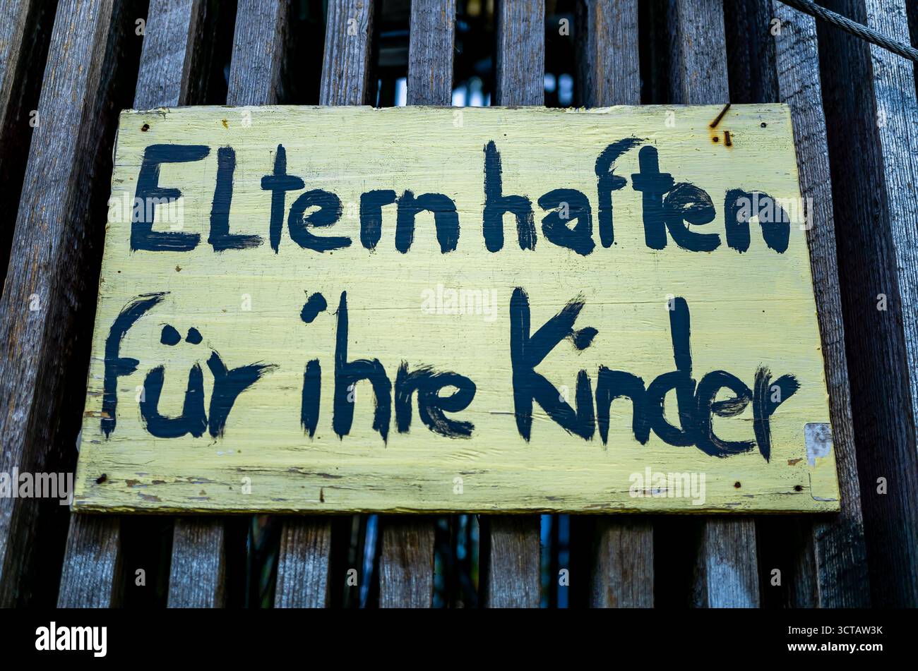 Gros plan d’une enseigne en bois jaune rustique avec texte allemand peint à la main “Eltern haften für ihre Kinder” sur une clôture en bois. Banque D'Images