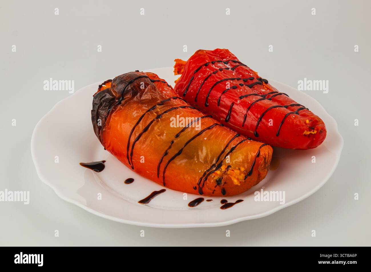 Les poivrons grillés colorés, un rouge et un orange, sont agencés avec goût sur une assiette blanche, rehaussés par un filet de vinaigre balsamique pour plus de saveur. Banque D'Images