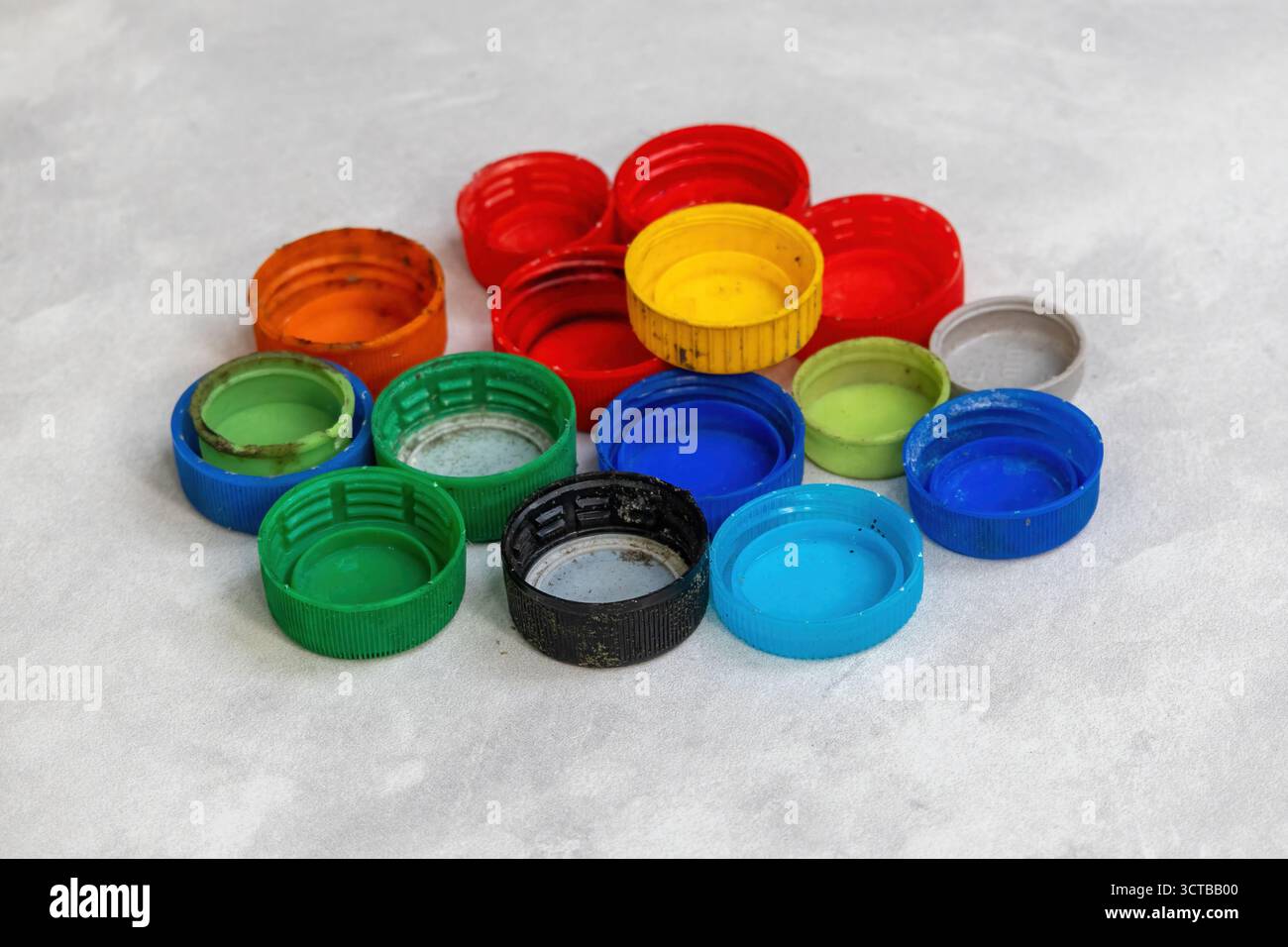 De nombreux bouchons de bouteilles en plastique colorés et assortis dispersés sur un sol en carreaux blancs. Gros plan pour le recyclage, l'upcycling, l'artisanat de bricolage créatif, les projets de réutilisation, un Banque D'Images