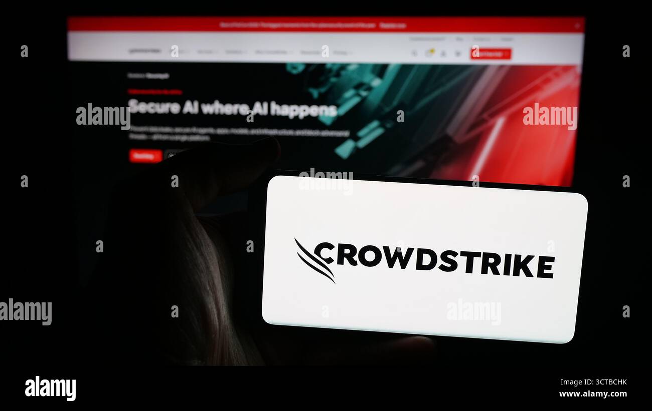 Dans cette illustration photo, une personne tient un téléphone portable avec le logo de la société de cybersécurité CrowdStrike Holdings sur l'écran devant la page Web. Banque D'Images