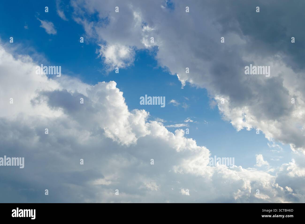 Une vue panoramique d'un ciel bleu vif rempli de grands nuages cumulus, illuminés par la lumière douce du soleil qui traverse, créant un paysage dramatique et paisible Banque D'Images