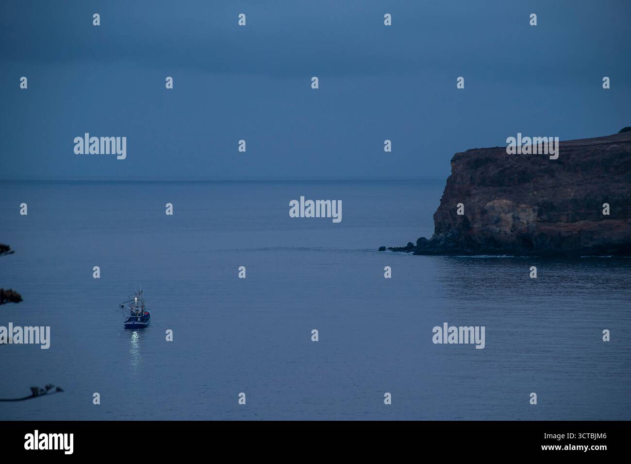 Un bateau flotte sur l'eau dans l'obscurité. L'eau est calme et le ciel nuageux Banque D'Images