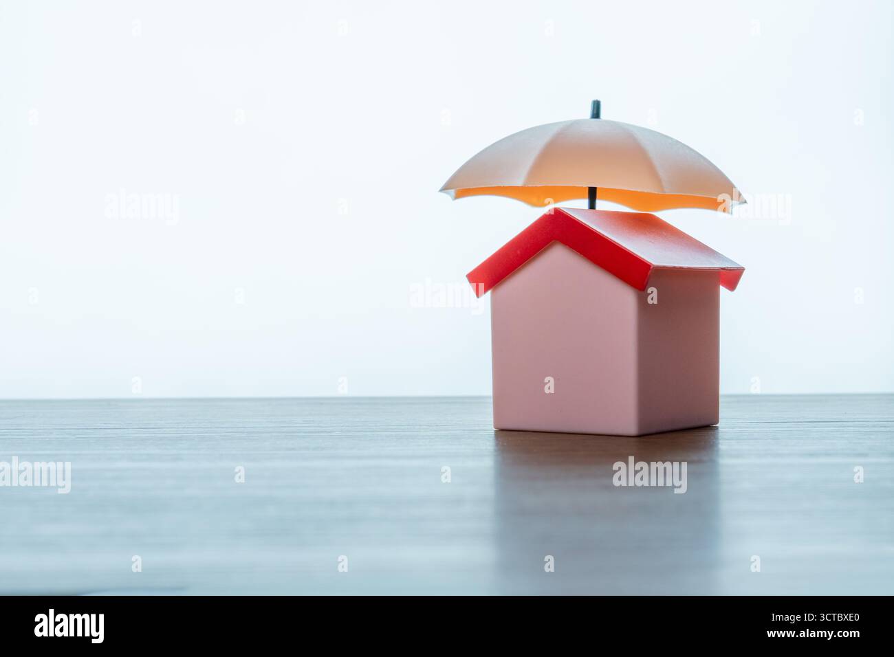 Une maison miniature protégée par un petit parapluie ouvert. Assurance habitation ou propriété, protection et concept de sécurité. Copier l'espace pour le texte. Banque D'Images