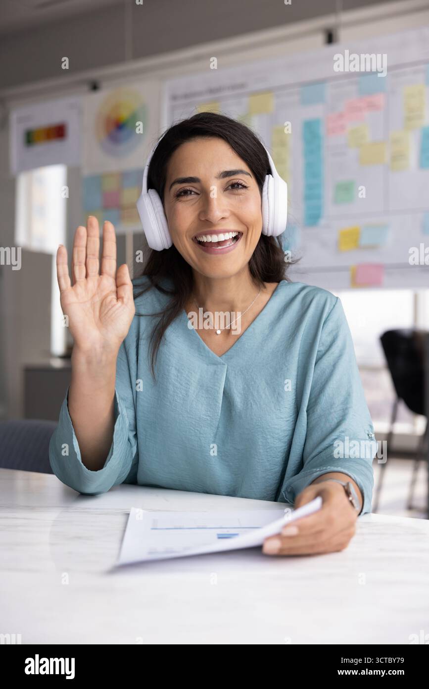 Positive amicale hispanique femme professionnelle portant des écouteurs, agitant la main bonjour Banque D'Images