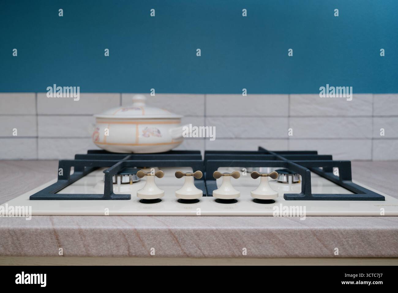Gros plan d'une table de cuisson à gaz beige avec une grille en fonte et un pot en céramique. Un poêle de cuisine moderne avec des poignées inhabituelles et une casserole de couleur claire sur Banque D'Images