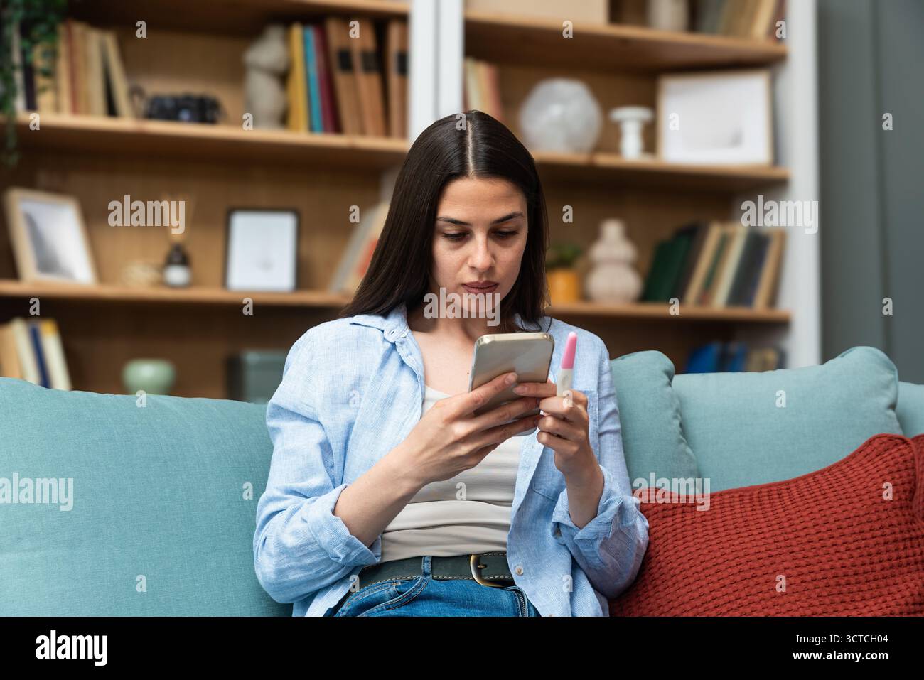 Jeune femme envoyant des SMS sur son smartphone tout en tenant un test de grossesse — en attendant les résultats, en envoyant des messages à un partenaire et en envisageant les prochaines étapes ; reproductif Banque D'Images