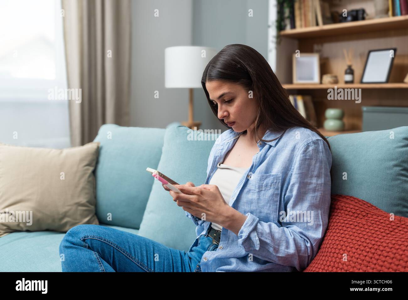 Jeune femme envoyant des SMS sur son smartphone tout en tenant un test de grossesse — en attendant les résultats, en envoyant des messages à un partenaire et en envisageant les prochaines étapes ; reproductif Banque D'Images