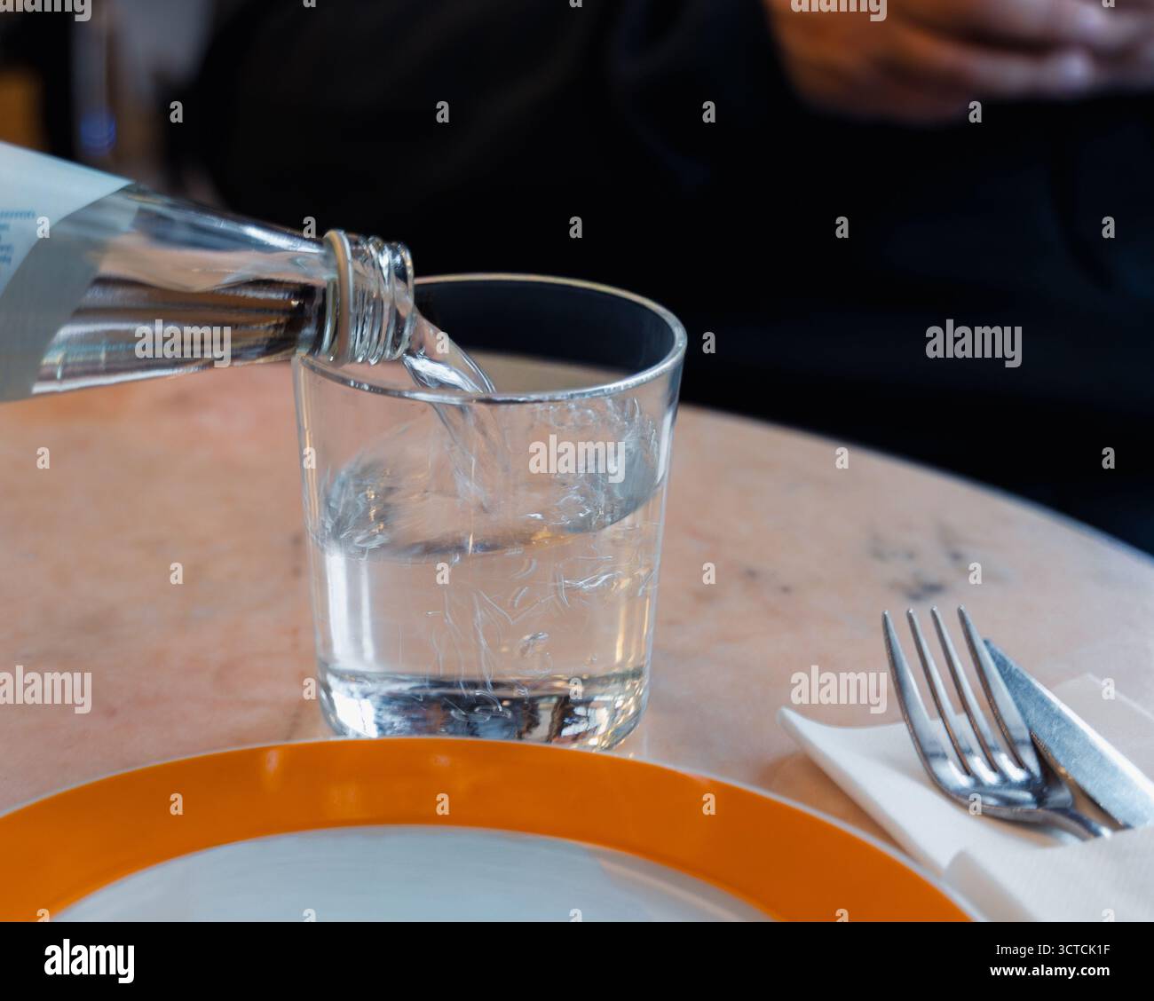 Gros plan de la main d'une femme versant de l'eau d'une bouteille en verre. Concentrez-vous sur l'hydratation, la santé et la durabilité dans la restauration et le style de vie Banque D'Images