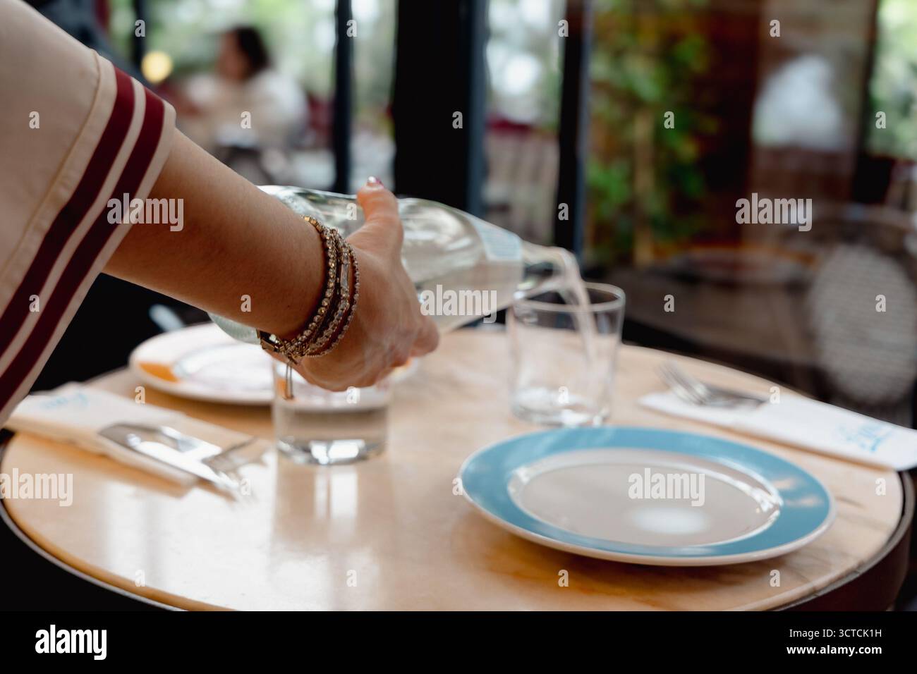 Gros plan de la main d'une femme versant de l'eau d'une bouteille en verre. Concentrez-vous sur l'hydratation, la santé et la durabilité dans la restauration et le style de vie Banque D'Images
