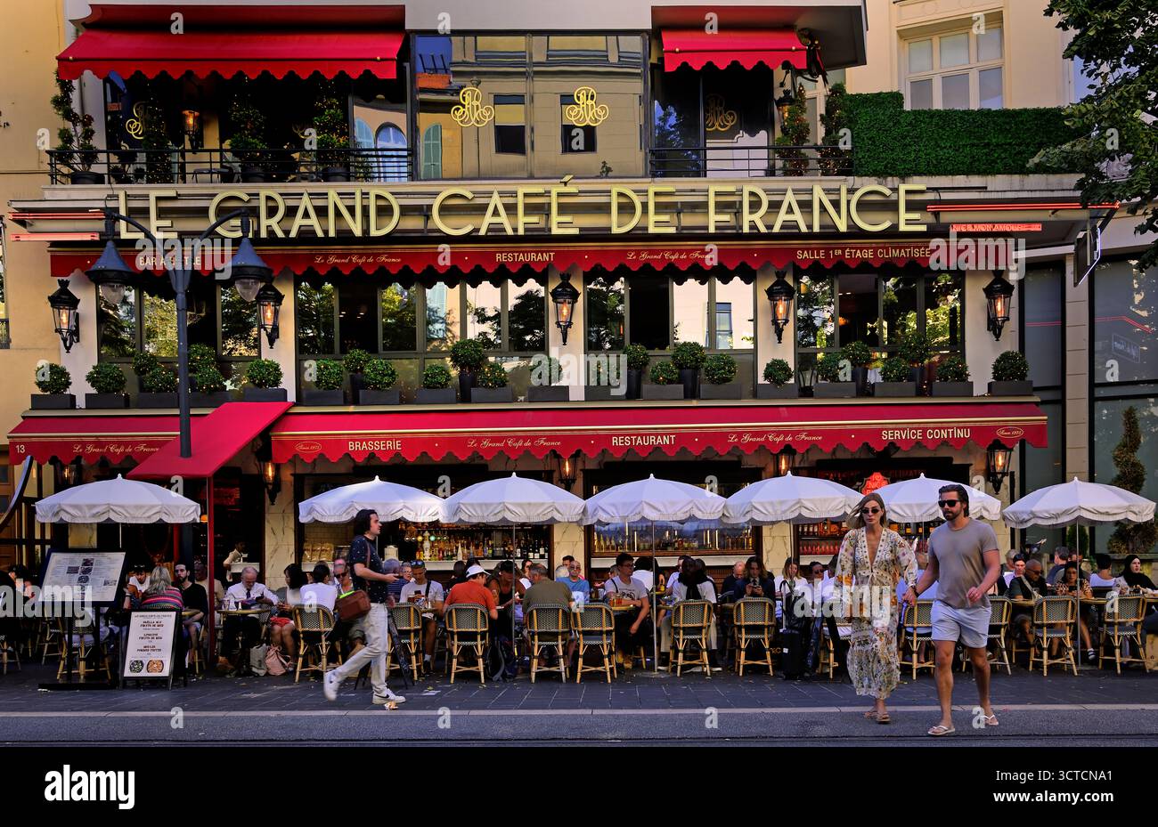 Les gens assis sur la terrasse extérieure de la brasserie le Grand Café de France avec ses auvents rouges emblématiques sur le Boulevard Jean Jaurès, Nice, Alpes-Maritimes Banque D'Images