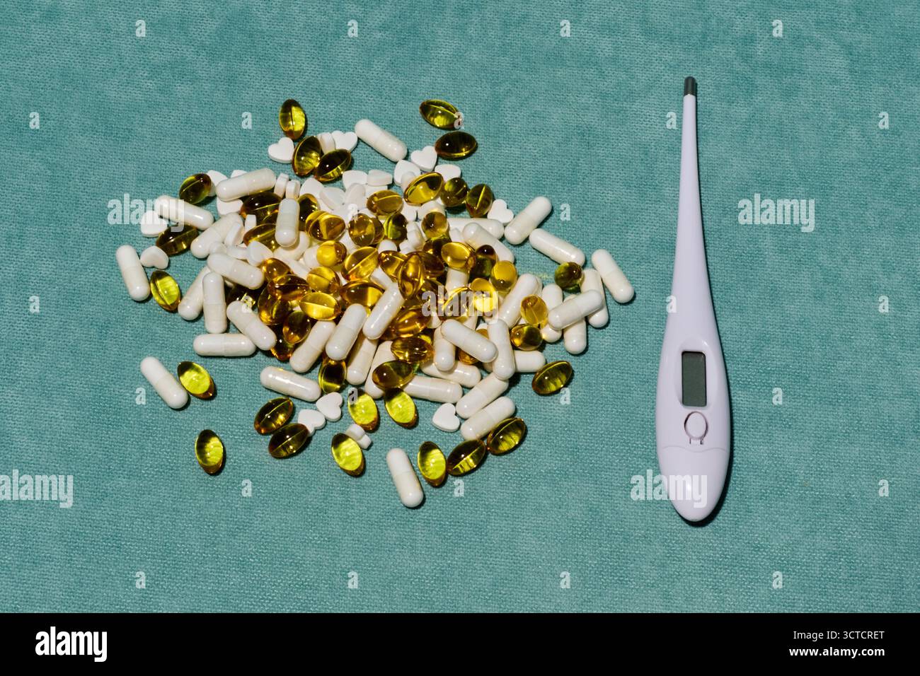 Nature morte médicale : thermomètre, capsules jaunes et blanches reposent sur un fond vert, symbolisant la santé et le traitement dans un cadre clinique Banque D'Images