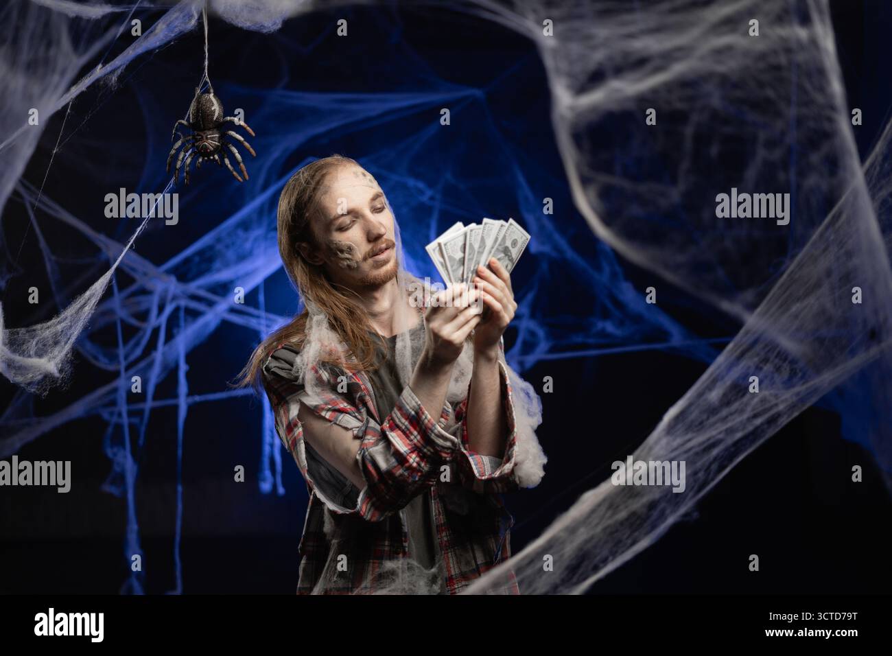 Effrayant homme zombie avec maquillage laid tenant de l'argent en espèces dans des billets de banque en dollars debout sur fond de toile d'araignée effrayant. Concept d'Halloween. Horreur fi Banque D'Images