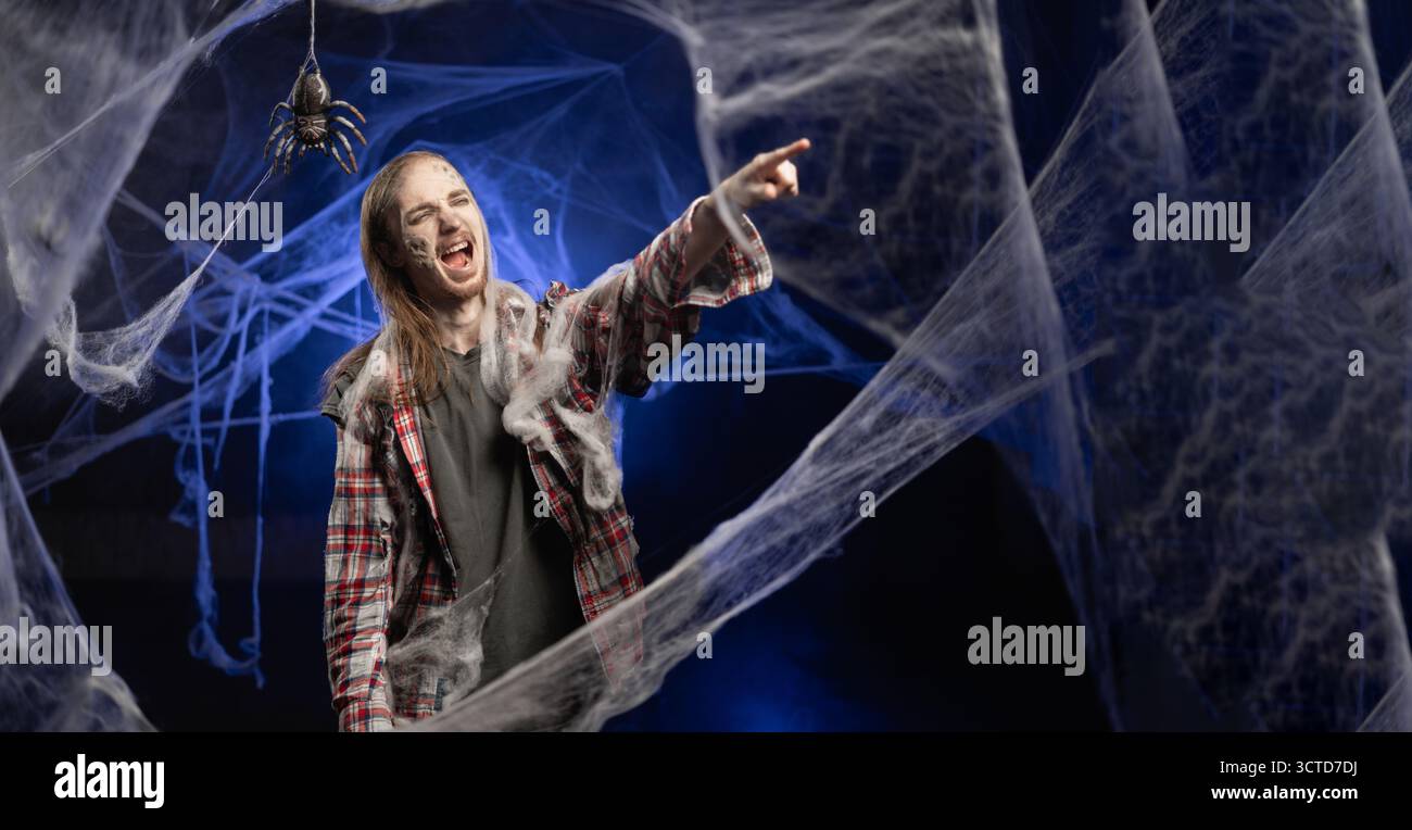 Mec mort avec horrible effrayant Halloween zombie maquillage sur le visage pointant les doigts, je vous choisis concept, publicité tout en se tenant couvert de toile d'araignée Banque D'Images