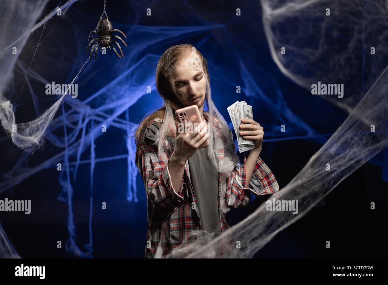 Mec mort avec horrible Halloween zombie effrayant maquillage sur le visage comptant des dollars argent misérable crédit d'épargne pauvre salaire debout couvert de toile d'araignée Banque D'Images