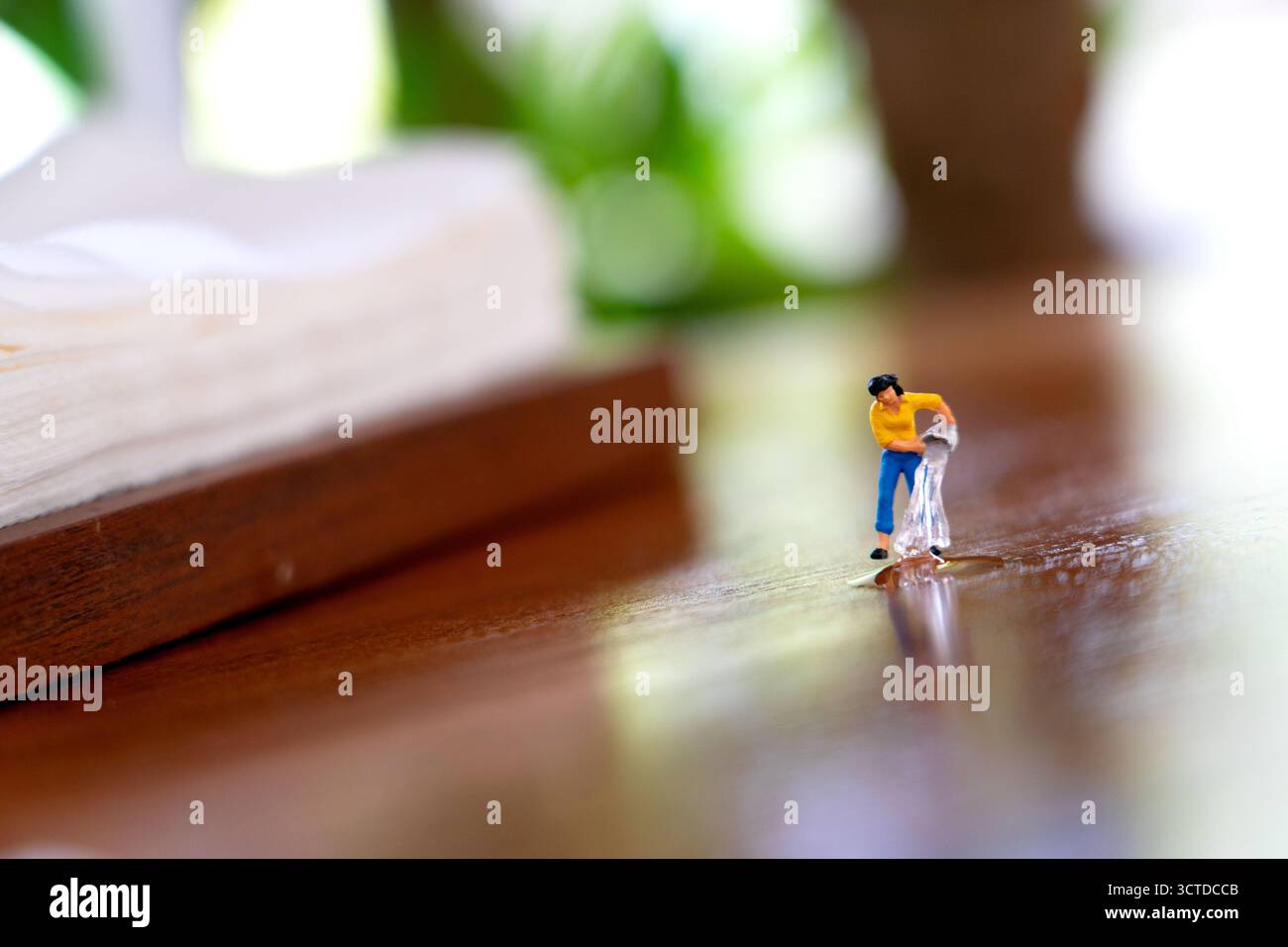 Figurine miniature verse de l'eau sur une surface en bois réfléchissante, mélangeant créativité ludique et narration imaginative dans une scène macro fantaisiste. Banque D'Images