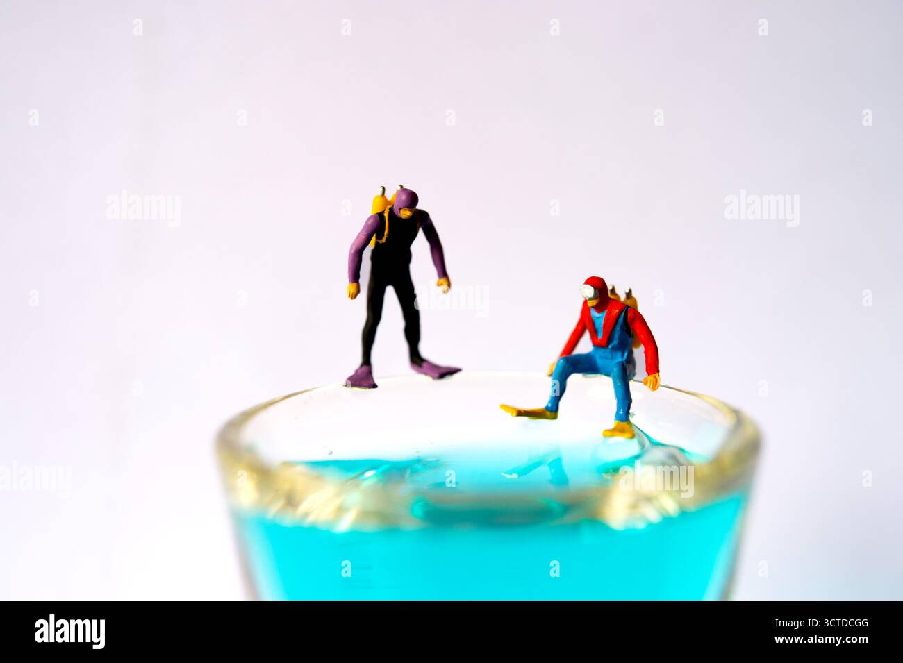 Tiny divers se prépare à l'aventure, debout sur le bord du verre rempli de liquide bleu - concept de photographie miniature créative Banque D'Images Tiny divers se prépare à l'aventure, debout sur le bord du verre rempli de liquide bleu - concept de photographie miniature créative Banque D'Images
