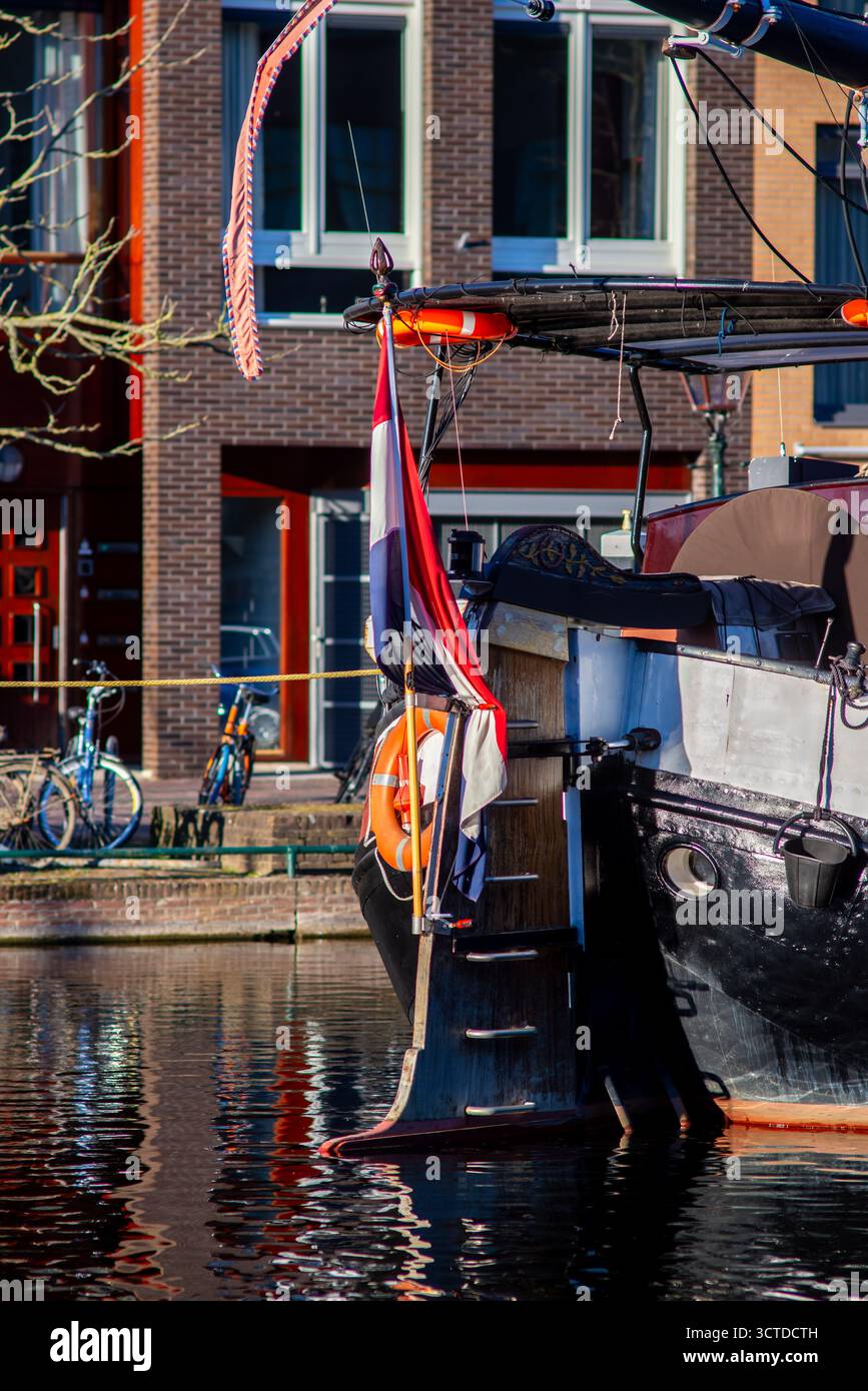 17.03.2025 Leyde, pays-Bas poupe d'un bateau historique amarré dans un canal à Leyde, pays-Bas, avec un drapeau néerlandais, bouée de sauvetage orange, gouvernail en bois, R. Banque D'Images