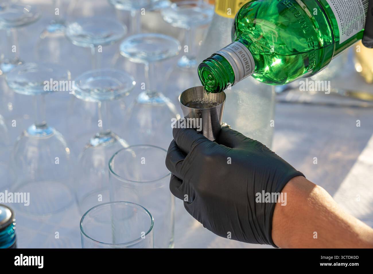 Détail du remplissage de gin shot dans la tasse à mesurer, barman porte un gant noir. Banque D'Images