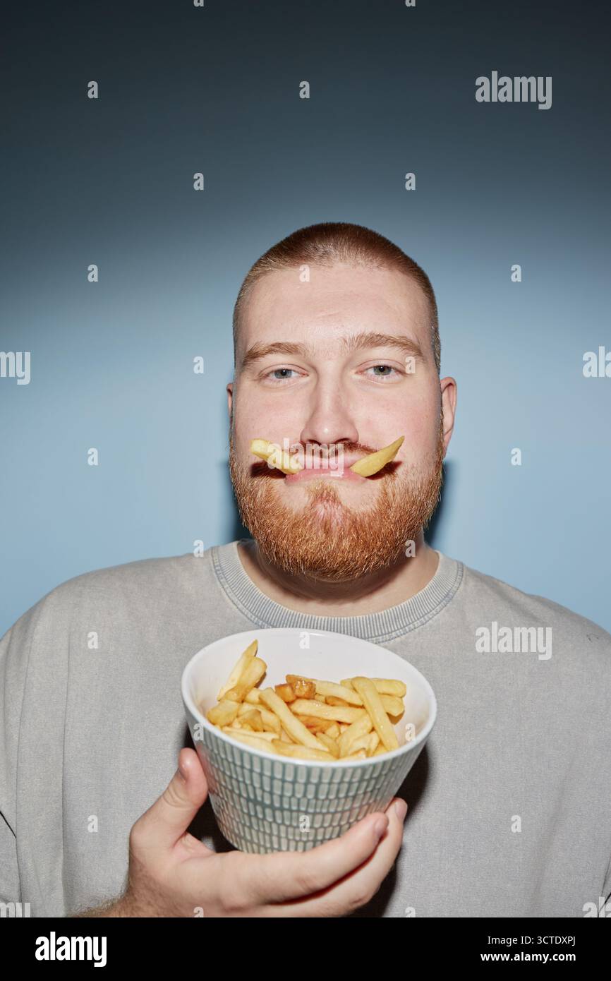 Portrait de jeune homme adulte tenant des frites et faisant le visage drôle Banque D'Images