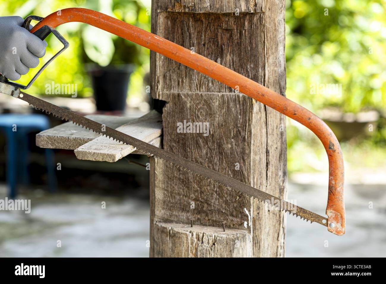 Une scie à main avec poignée orange est utilisée pour couper le poteau en bois à l'extérieur, présentant le projet de menuiserie diy. l'arrière-plan est flou Banque D'Images