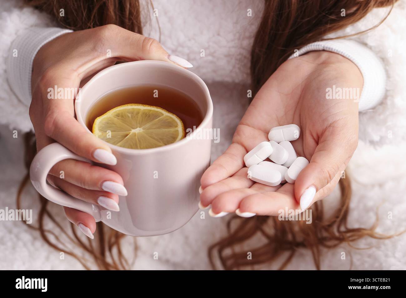 Femme tenant une tasse de thé et des pilules blanches dans les mains. Concept de traitement du rhume et de la grippe. Boisson chaude pour le confort et la récupération pendant la maladie. Banque D'Images