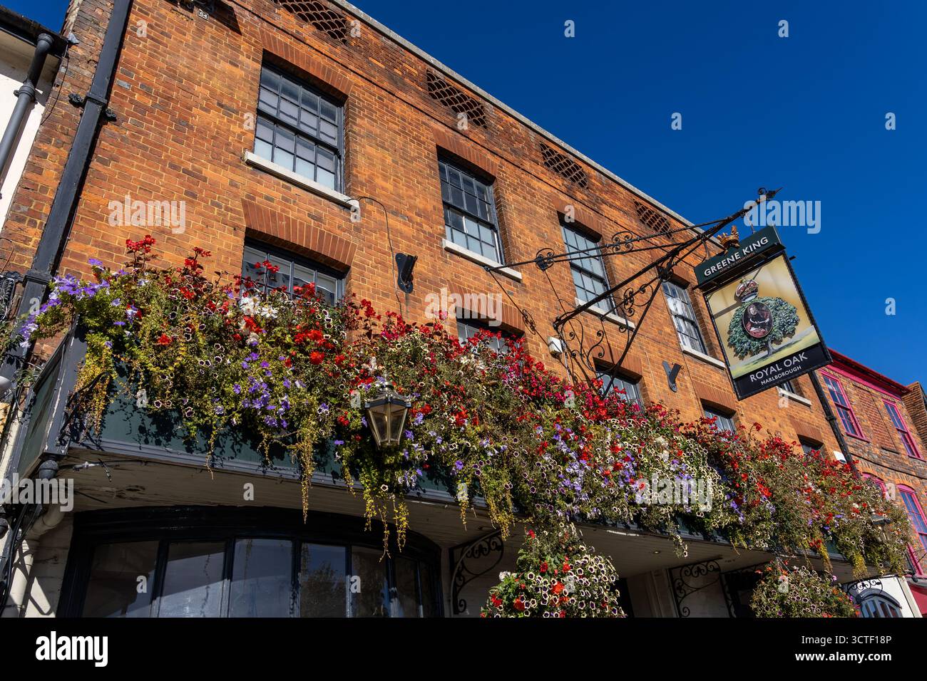 Bâtiment historique en brique rouge le pub Royal Oak avec panneau suspendu Marlborough High Street orné de fleurs suspendues vibrantes sous un ciel bleu clair Banque D'Images