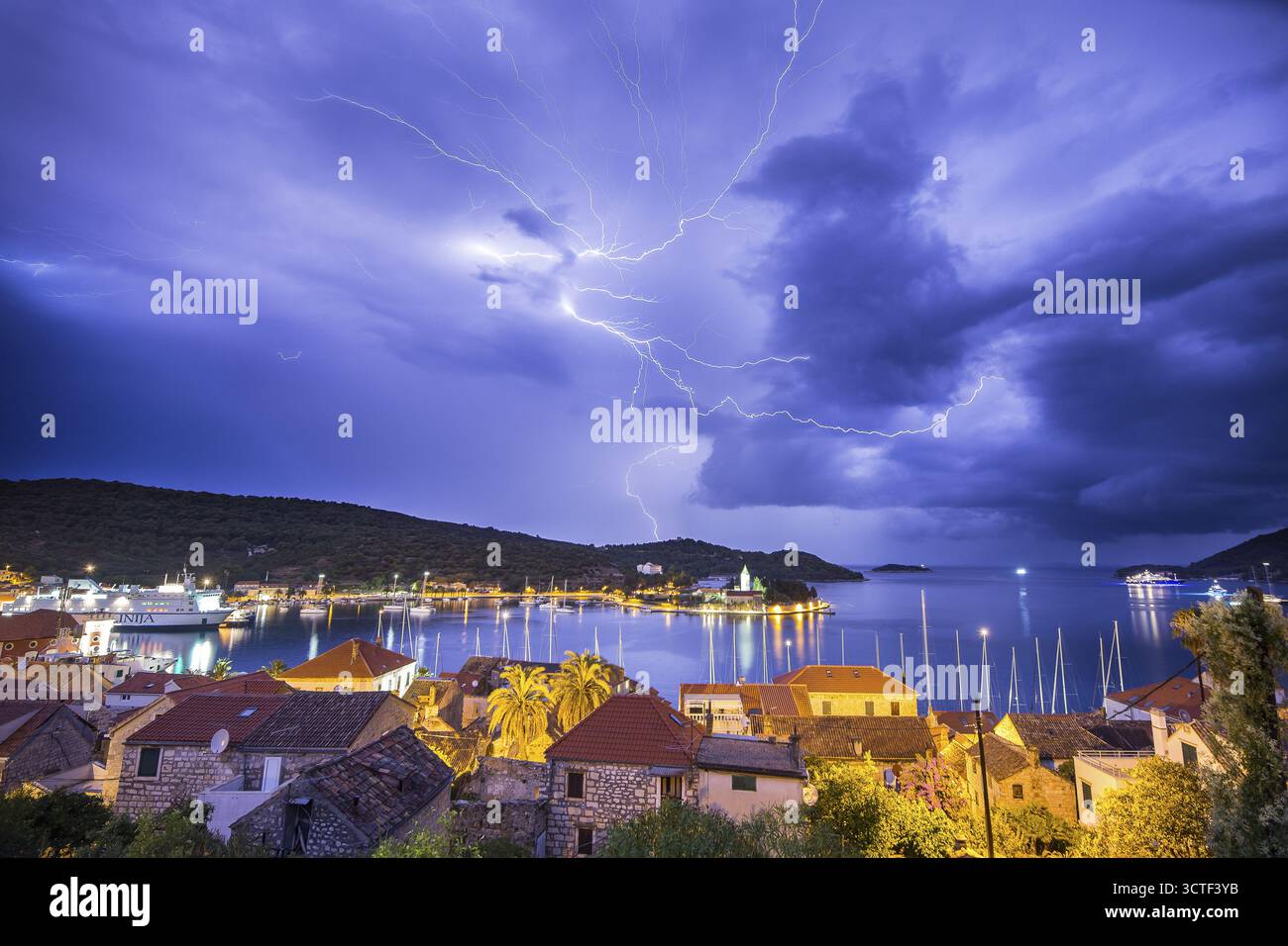 Vue de déchirures de foudre spectaculaires à travers le ciel nocturne au-dessus des eaux calmes reflétant les lumières de la ville, éclairant la ville, vis, Split-Dalmatie County, Banque D'Images