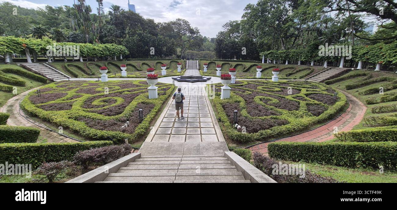 Une personne se promène dans un jardin botanique magnifiquement entretenu avec des haies complexes et des sentiers centraux - Kuala Lumpur, Malaisie Banque D'Images