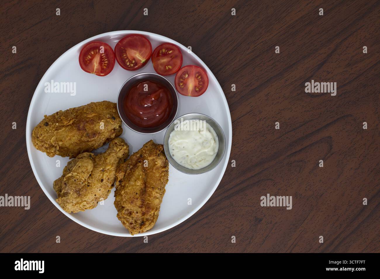 Ailes de poulet frites avec ketchup et tomates cerises sur une assiette blanche Banque D'Images