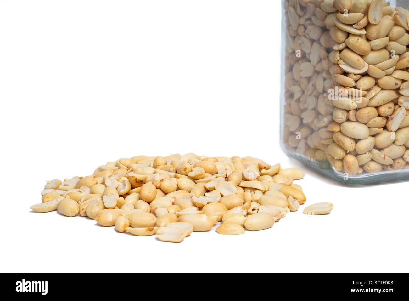 Cacahuètes écaillées renversant du pot en verre sur fond blanc isolé. Gros plan des arachides avec pot. Concept de nutrition, santé et collation Banque D'Images