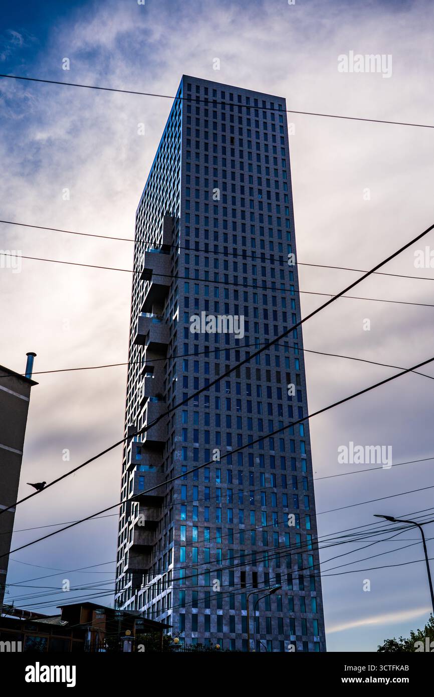 Gratte-ciel moderne à Tirana Albanie avec façade en verre et design géométrique contre un ciel nuageux et des lignes électriques croisées Banque D'Images