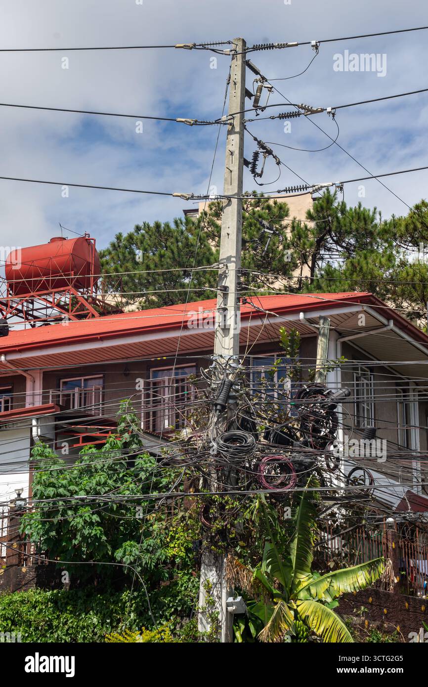 Maison avec un réseau complexe et enchevêtré de fils électriques, probablement pour l'électricité et les télécommunications, sur un poteau électrique, Baguio, Philippines Banque D'Images