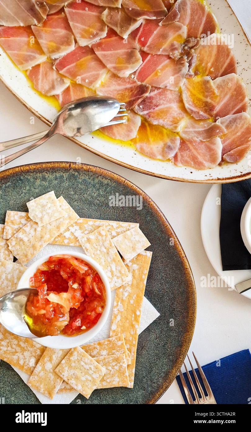 Un plat gastronomique élégant présente de la viande séchée finement tranchée sur une assiette blanche, avec des craquelins croustillants et un bol de salsa de tomates fraîches, parfait pour le Sharin Banque D'Images