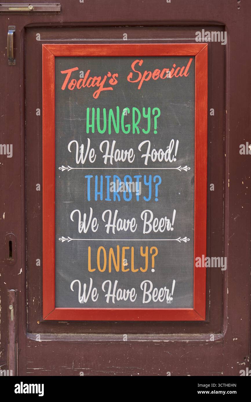 Panneau coloré au tableau noir avec texte humoristique à l'extérieur d'un pub ou d'un restaurant, offrant de la nourriture et de la bière pour les voyageurs affamés Banque D'Images