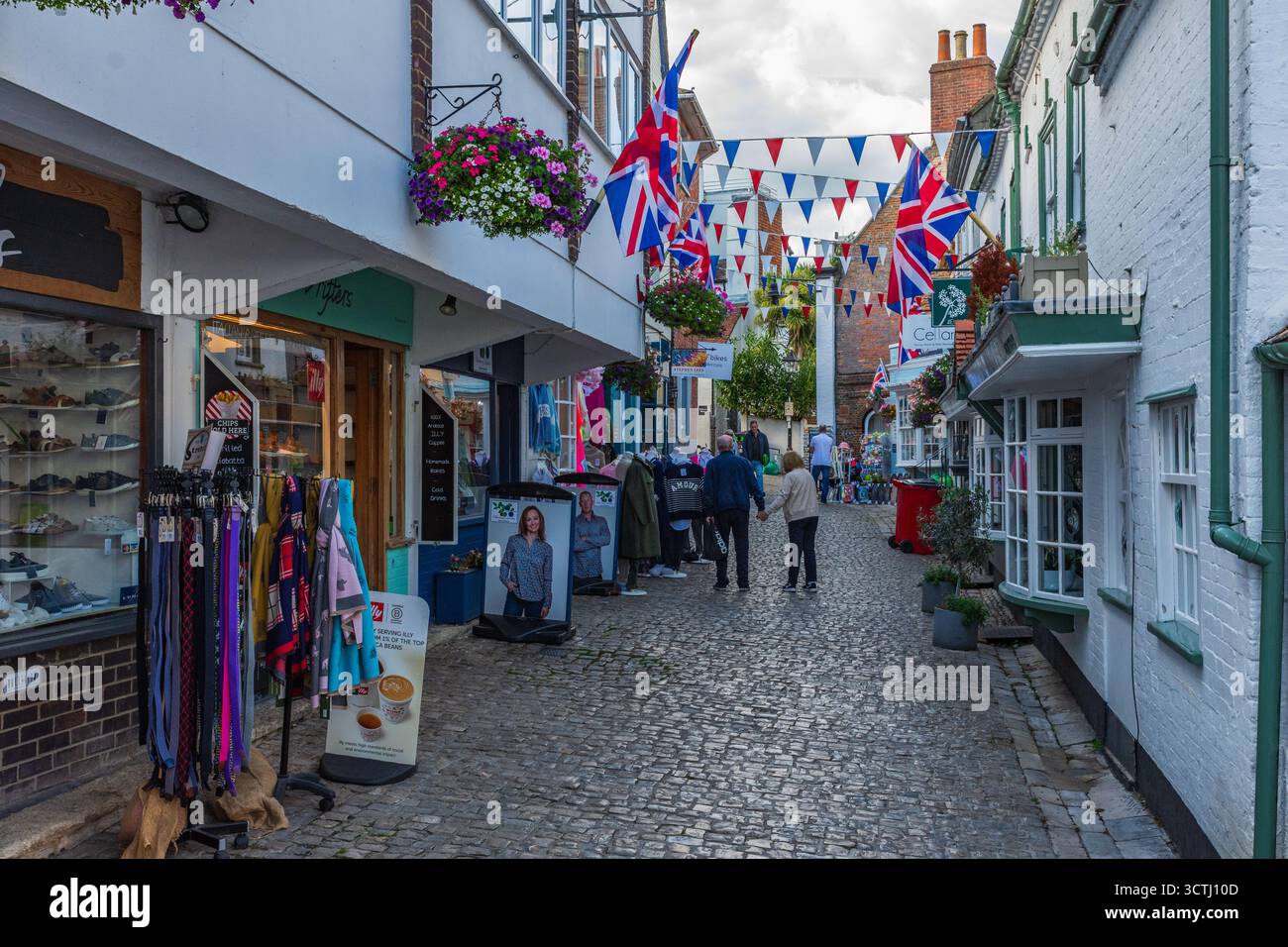 Quay Street, Lymington, Royaume-Uni - 29 septembre 2025 : People une rue de magasins dans des bâtiments classés grade II avec des banderoles et des drapeaux Union Jack. Banque D'Images