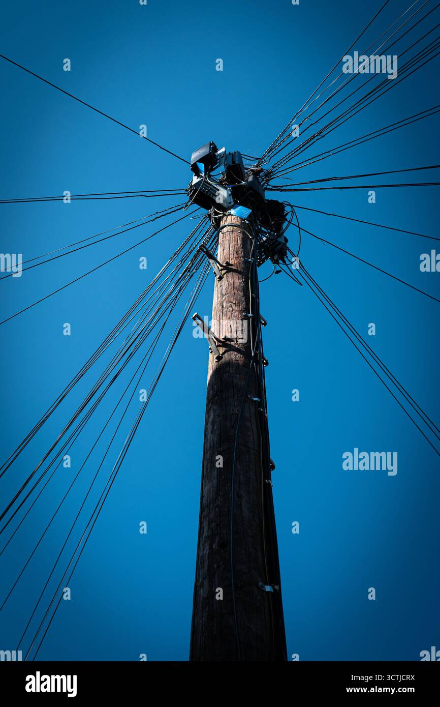 Poteau télégraphique avec de nombreux fils rayonnants contre un ciel bleu clair Banque D'Images