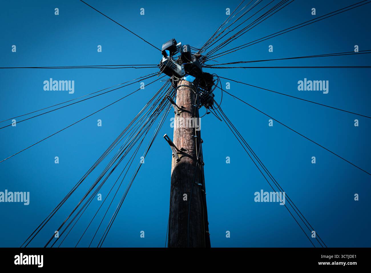 Poteau télégraphique avec de nombreux fils rayonnants contre un ciel bleu clair Banque D'Images