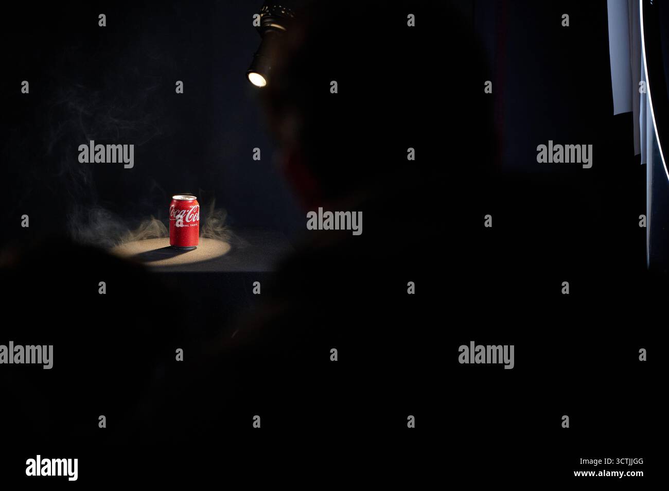 Canette de coca-cola éclairée entourée de fumée sur une table noire avec des silhouettes de spectateurs, photographie de produit studio à usage commercial Banque D'Images