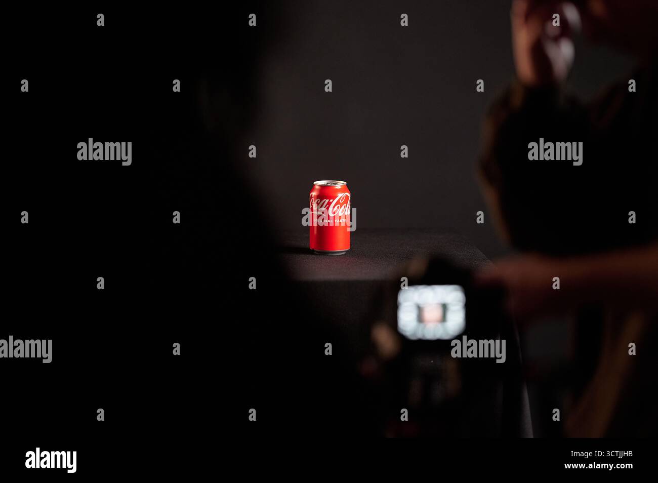 Canette de coca-cola éclairée entourée de fumée sur une table noire avec des silhouettes de spectateurs, photographie de produit studio à usage commercial Banque D'Images